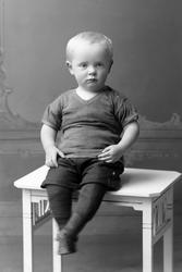 Studioportrett av en gutt sittende på et bord.