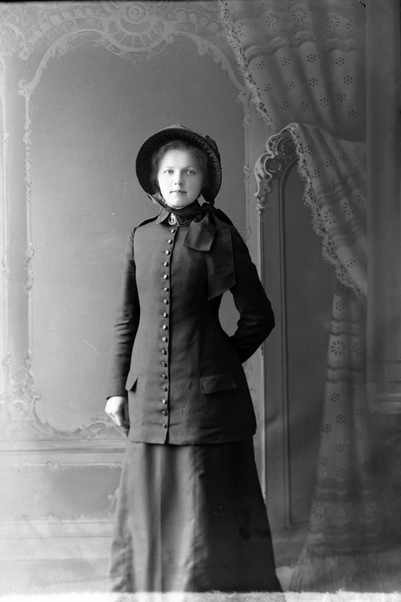 Studioportrett av en ung kvinne med jakke og hatt.