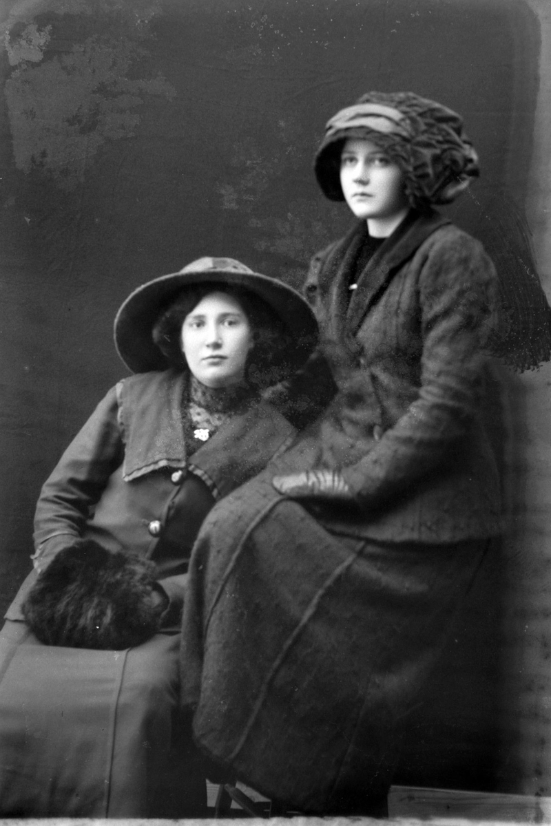 Studioportrett av to kvinner med hatter på hodet.