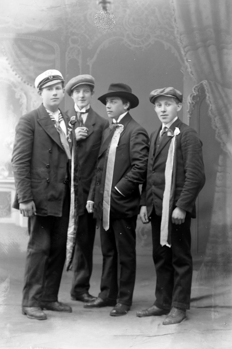 Studioportrett av fire unge menn med sløyfer på brystet.