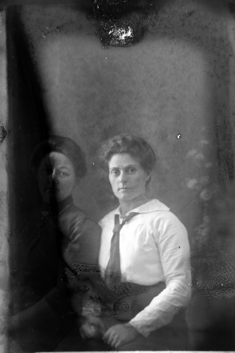 Studioportrett av to kvinner som sitter. Bildet skjuler delvis den ene kvinnen.