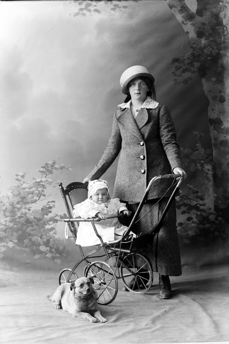 Studioportrett av en kvinne med et barn i barnevogn og en hund.