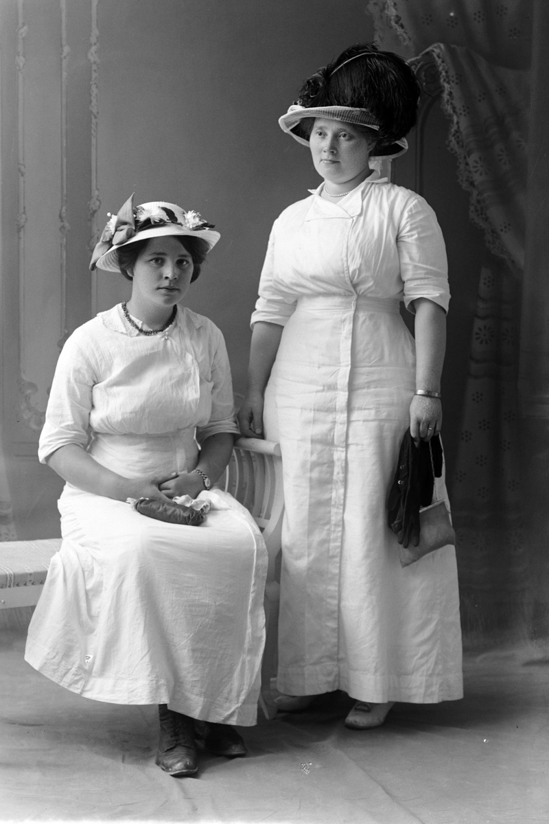 Studioportrett av to kvinner i hvite kjoler.