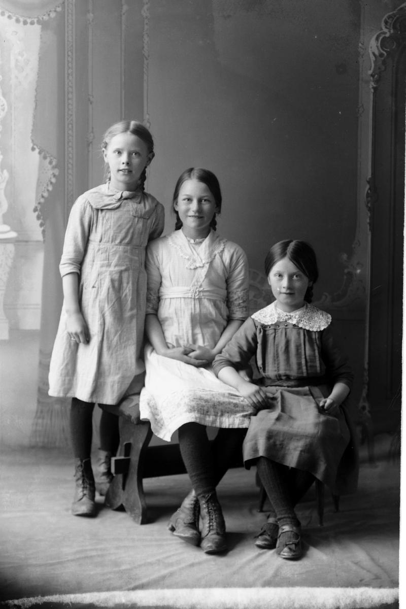 Studioportrett i helfigur av tre unge jenter.