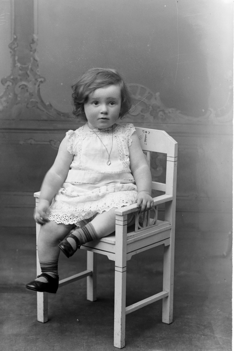 Studioportrett av en liten jente sittende på en stol.