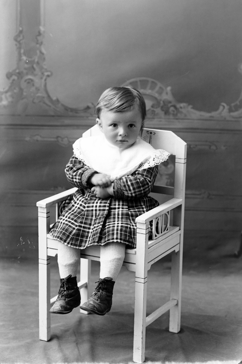 Studioportrett av et lite barn sittende på en hvit stol.