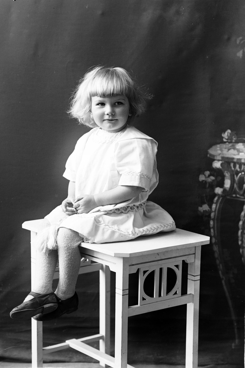 Studioportrett av en liten jente i hvit kjole.
