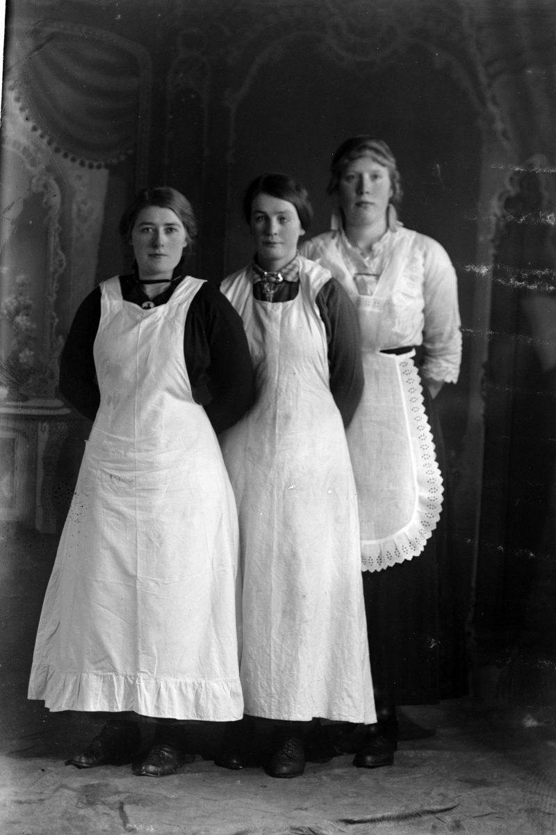 Studioportrett av tre kvinner som har på seg forklær.