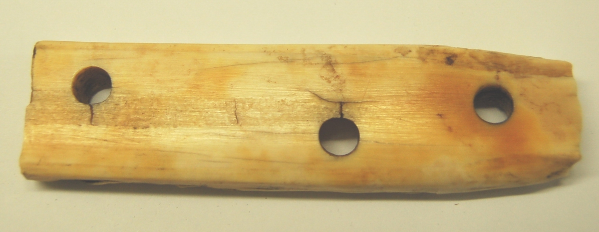Skinnedel av elfenbein fra kvalross til bruk under meier på sleder. Gjenstanden har hull for festing til tremeien, anten med beinnagler eller reimer. 