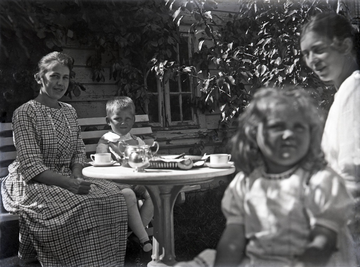 Eksteriør - Familiegruppe. To kvinner og to barn nyter kaffe og mat på verandaen