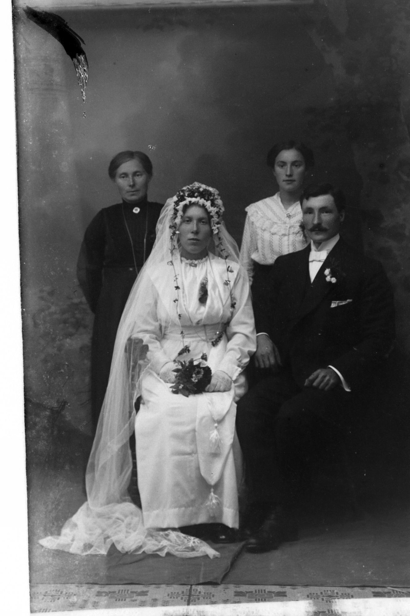 Studioportrett av et brudepar med familie eller gjester stående bak seg.