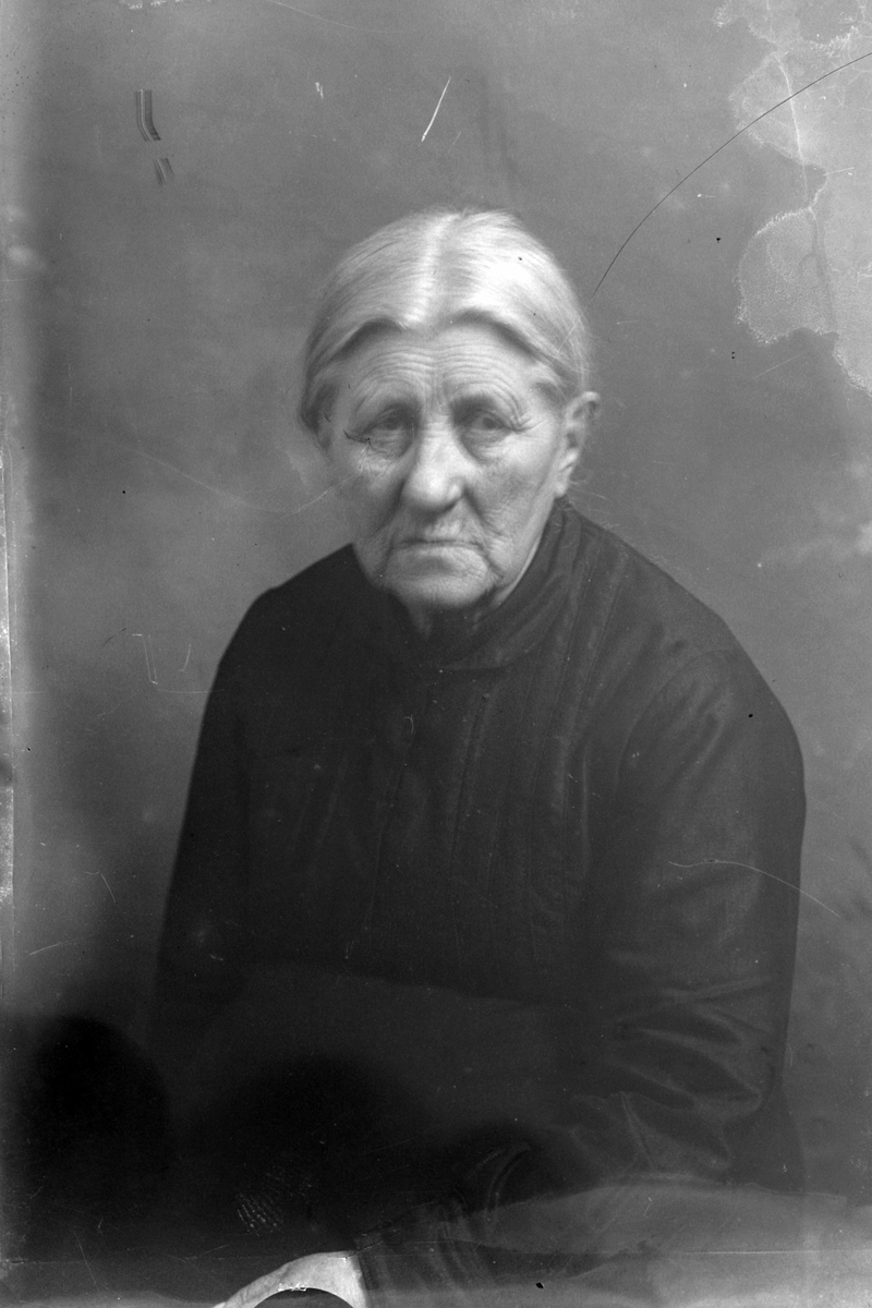 Studioportrett av en eldre kvinne i en mørk kjole.