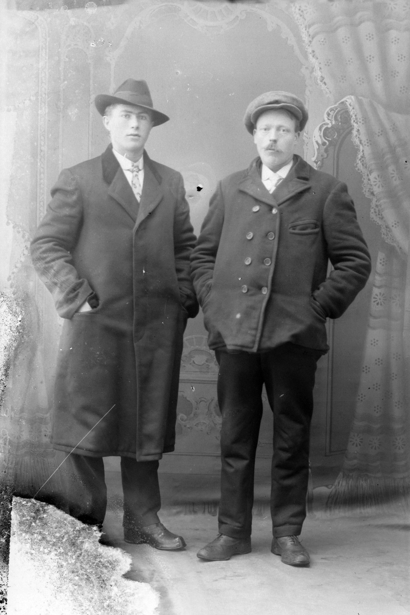 Studioportrett av to menn med henderne i lommene sine.