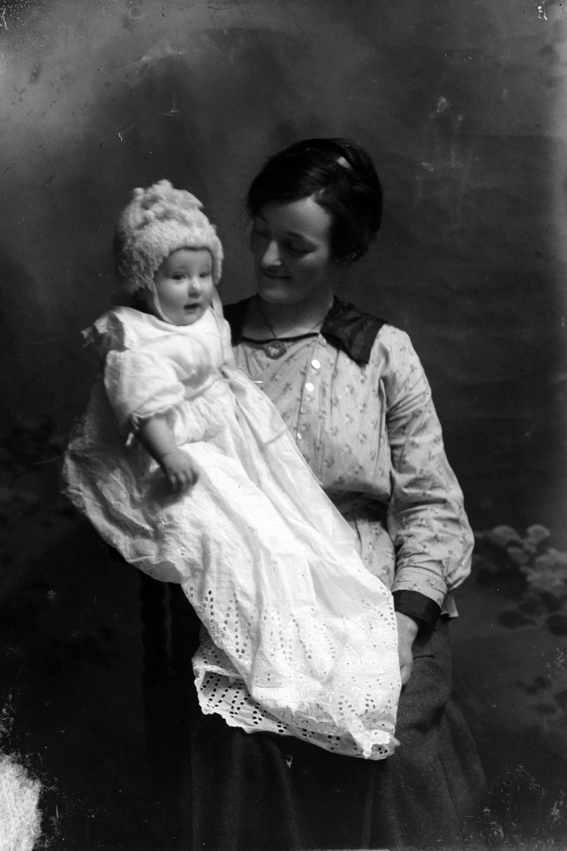 Studioportrett av en kvinne med barn i dåpskjole på fanget.