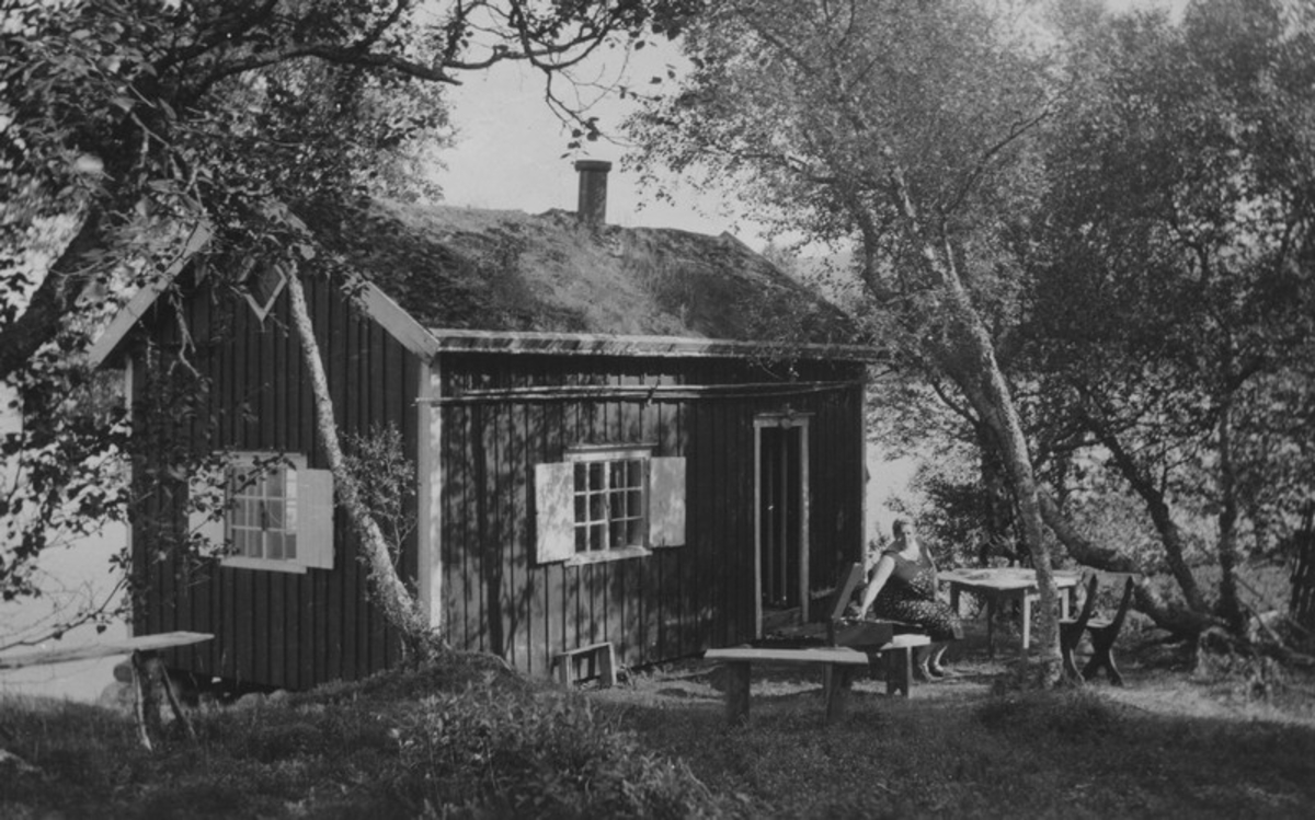 På hytta, "huskestua", ved Kilvatnet der Normanfamilien hadde hytte. Den ble bygd i 1916.
Aagot Olausssen sitter utenfor ved et bord.