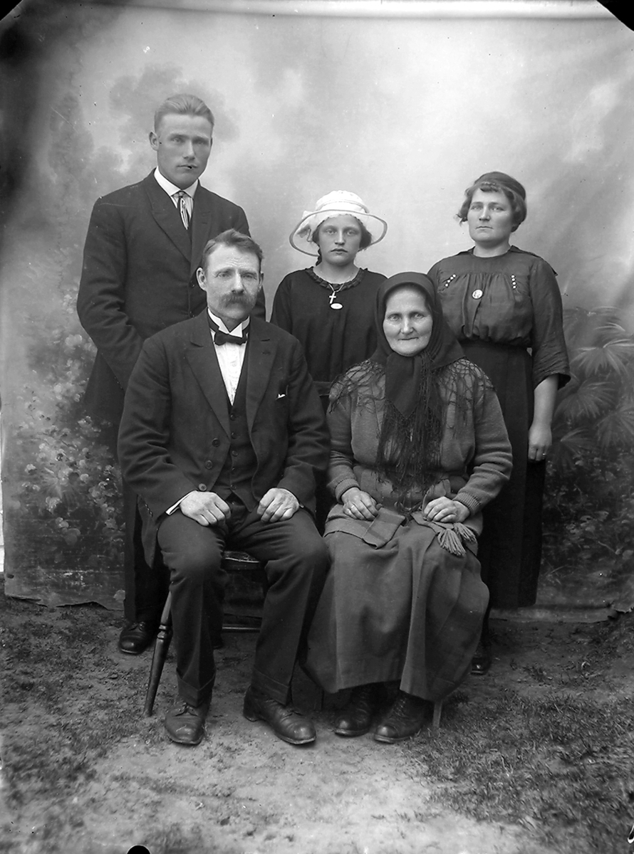 Portrett. Familiebilde. 5 personer.Foran sitter et par i 70-80-åra, kvinnen med tørkle. Bak står et par i 30-40-åra og ei jente i tenårene, jenta med hatt.Bildet er tatt i Beiarn.