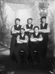 Gruppebilde. 5 menn med armene i kors To sitter. Tre står. C