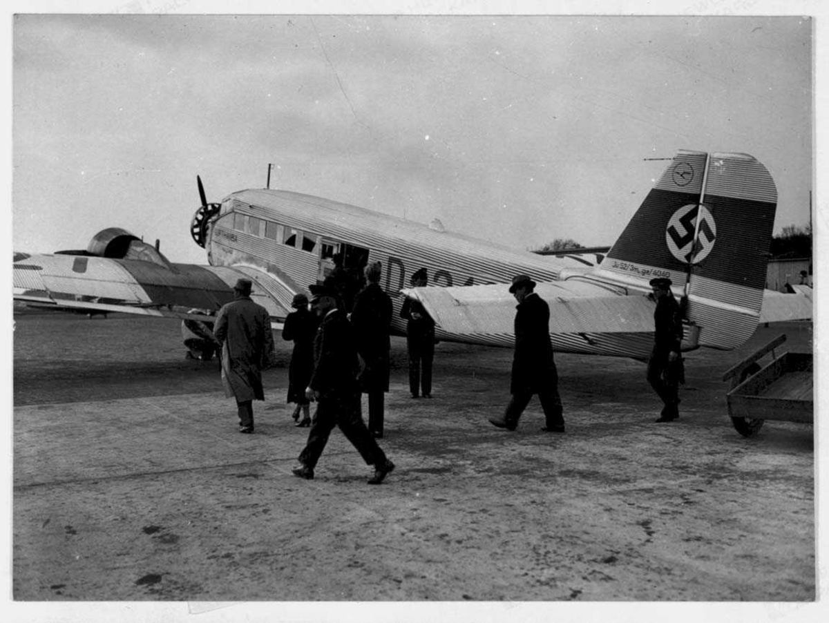 Lufthavn. Ett fly på bakken, Junkers Ju52, D-3127 "Otto Parschau" fra Lufthansa.. Hakekors på haleroret. Flere personer ved flyet.