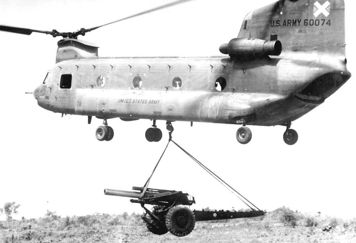 1 helikopter i luften med en kanon hengende under seg. Boeing Vertol 114 CH-47 Chinook.