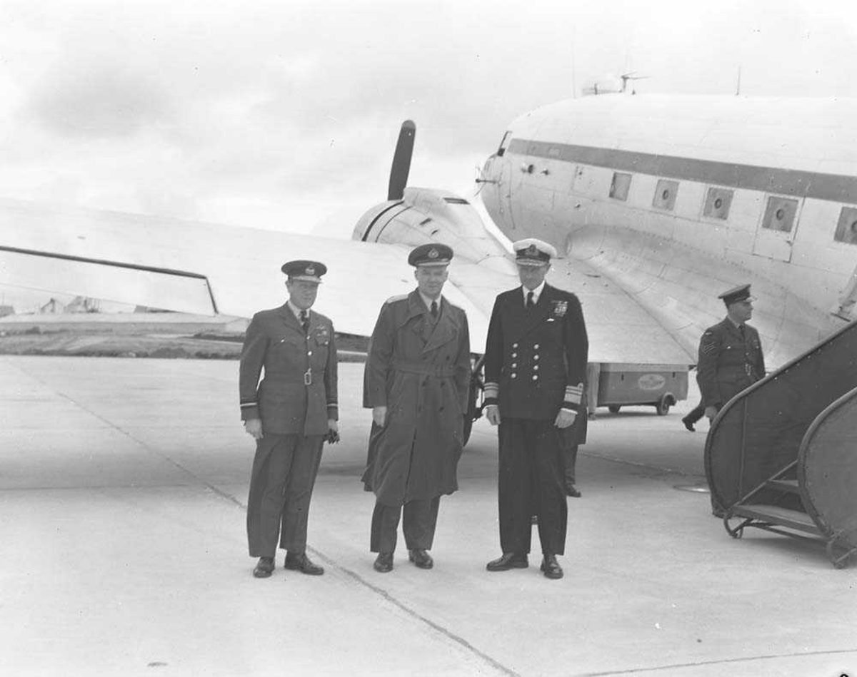 Lufthavn. Fire personer (militært personell) foran et fly