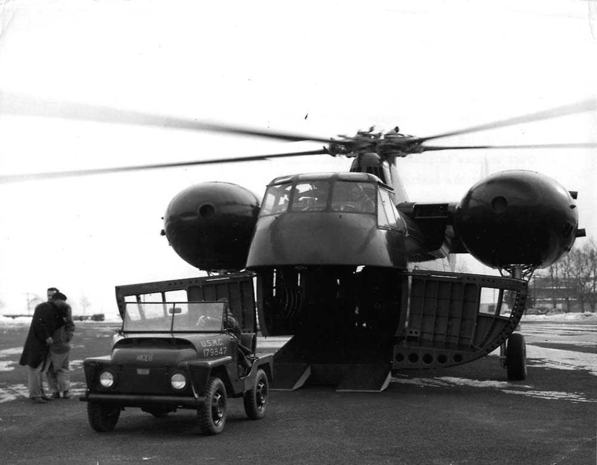 Ett helikopter på bakken med åpen lasteluke, Sikorsky S-56 CH-37 Mojave. Et kjøretøy med en person oppi står foran helikoptret, to personer står ved siden av.