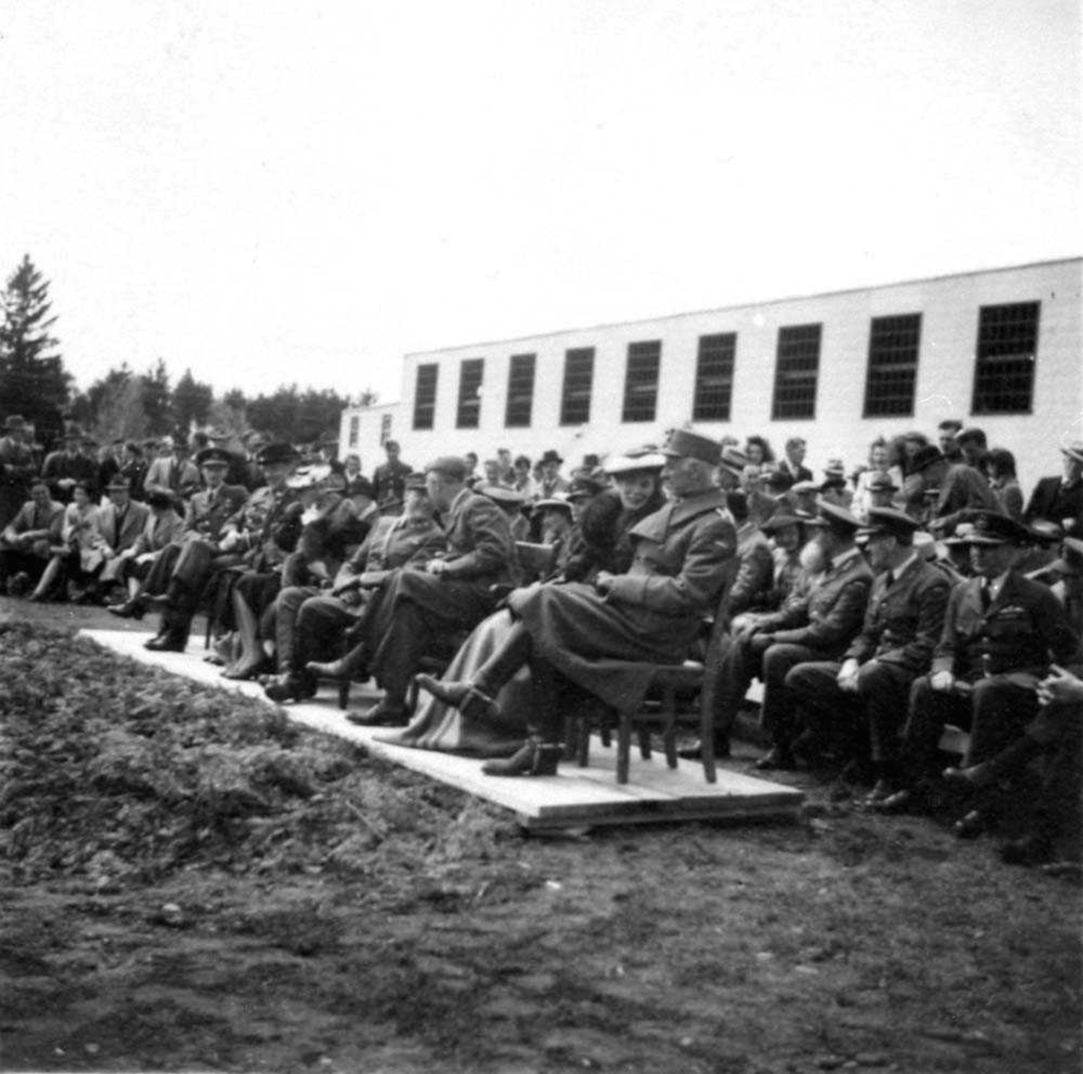Gruppefoto. En gruppe personer som sitter foran en bygning, mange i militæruniform.