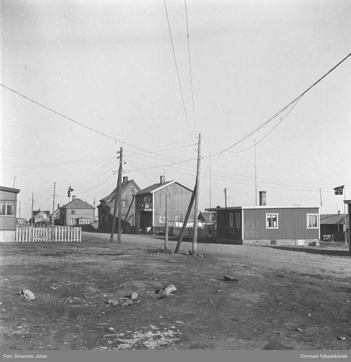 Et gateparti fra Damsveien i Vadsø. Bungalover. Den første bungaloven fra venstre hører til Torvald Berg og den andre til Gandola.  Fremst på bildet grusvei og to strømstolper.