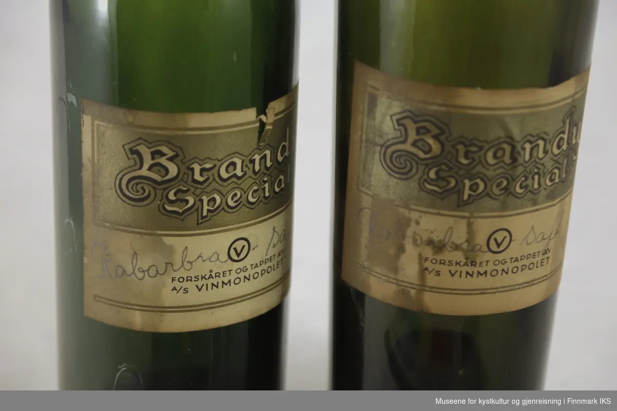 Flaskene er utført i mørkt grønt glass med etiketter i beige, gull og sort. Den ene flaska har brattere overgang fra kropp til flaskehals enn den andre. Etikettene er merket med produkt- og produsentnavn og teksten "Rabarbrasaft 1948" er påført for hånd.