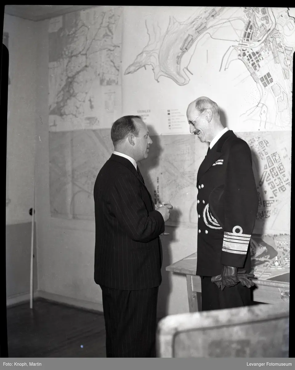 Kong Haakon med  kart og modell over Steinkjer, i samband med gjernreisningen i Steinkjer etter at byen ble bombet.
