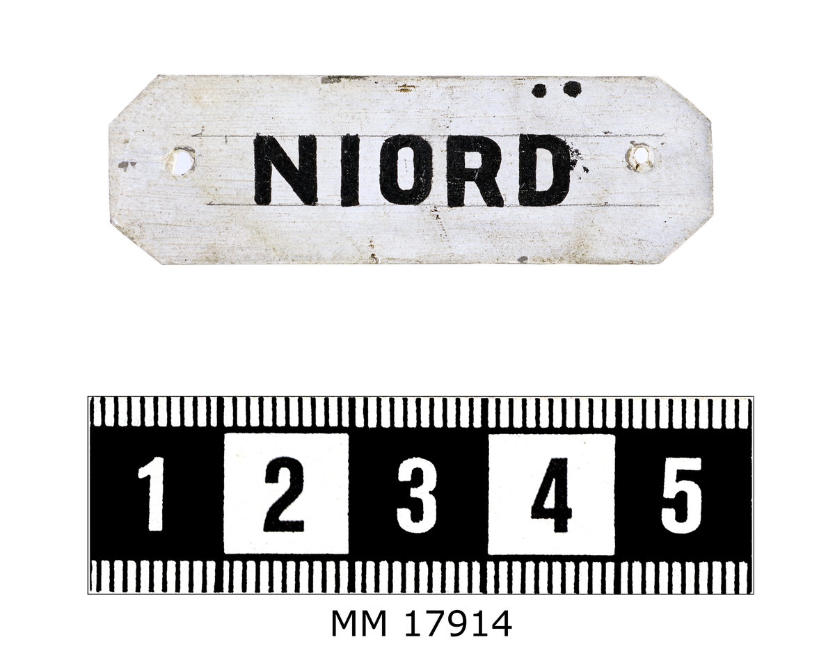 Rektangulär skylt av plåt med avklippta hörn. Framsidan vitmålad och försedd med handmålad text i svart: " NIORD ". Hål i kanterna för spikar.