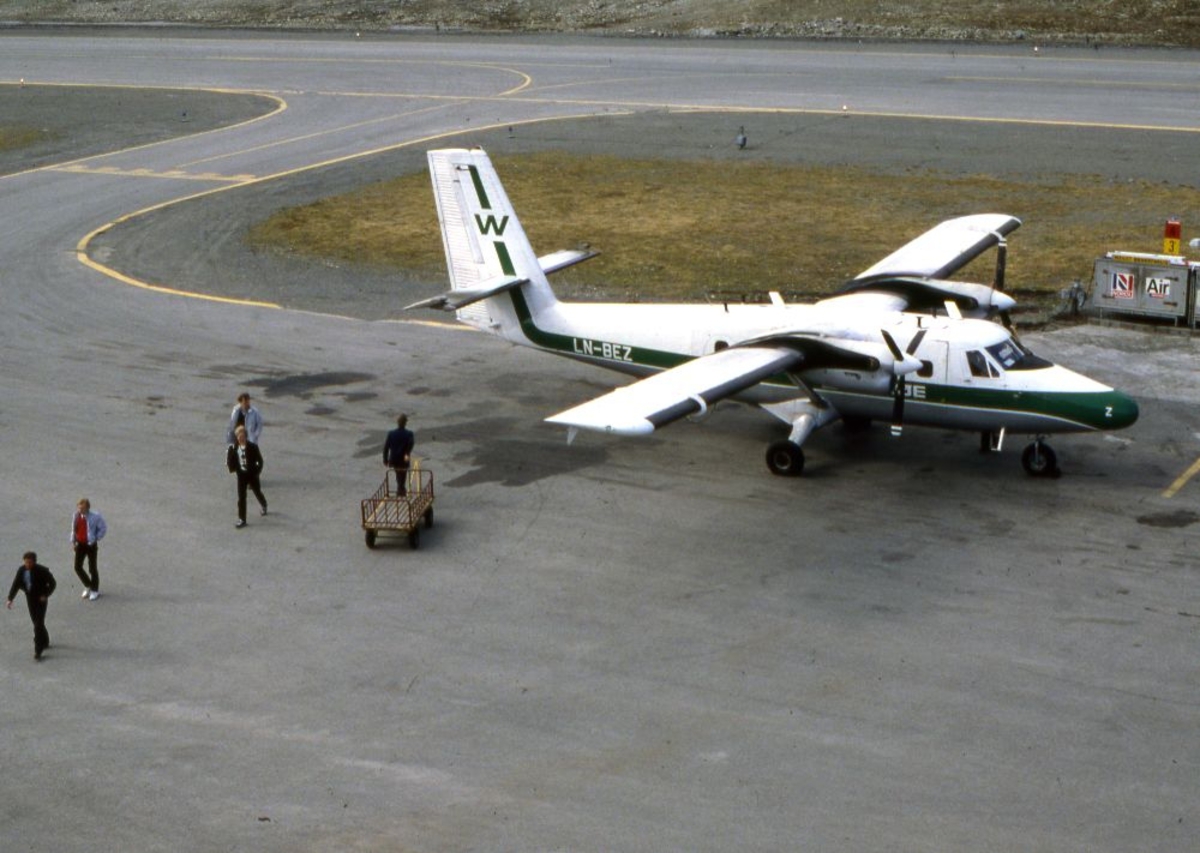 Lufthavn (flyplass). Et fly, LN-BEZ, DHC-6-300 Twin Otter fra Widerøe parkert. Passasjerer forlater flyet og en person med bagasjevogn mot flyet.
