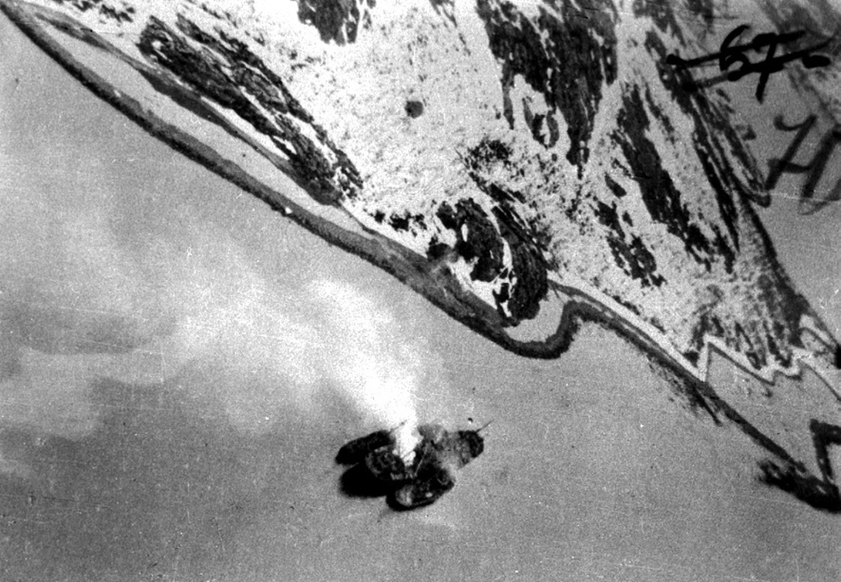 Luftfoto, 3 fartøy nedenfor, et større og to mindre somm ligger ved siden av hverandre. Røyk stiger opp fra dem etter bombetreff. Landskap bak.