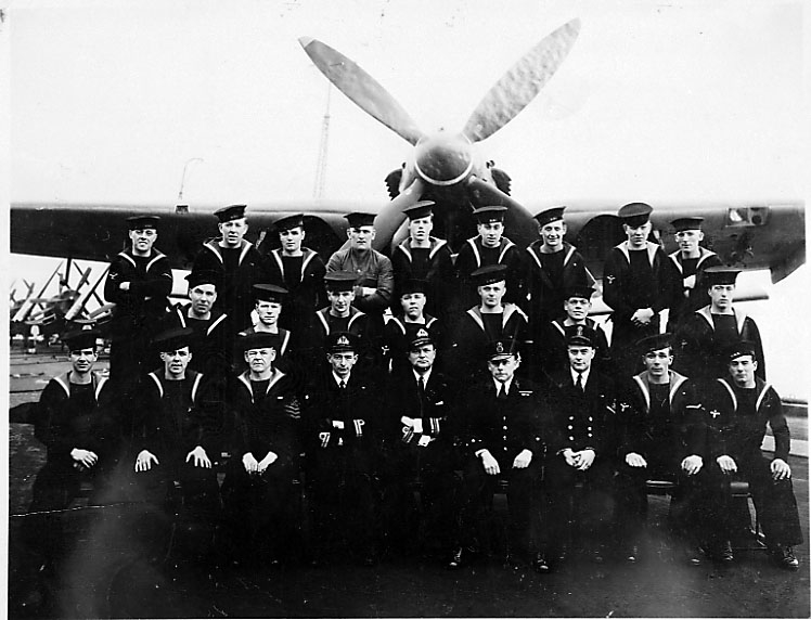 Portrett, gruppefoto av personer i militæruniform. 1 fly i bakgrunnen, Baracuda.
