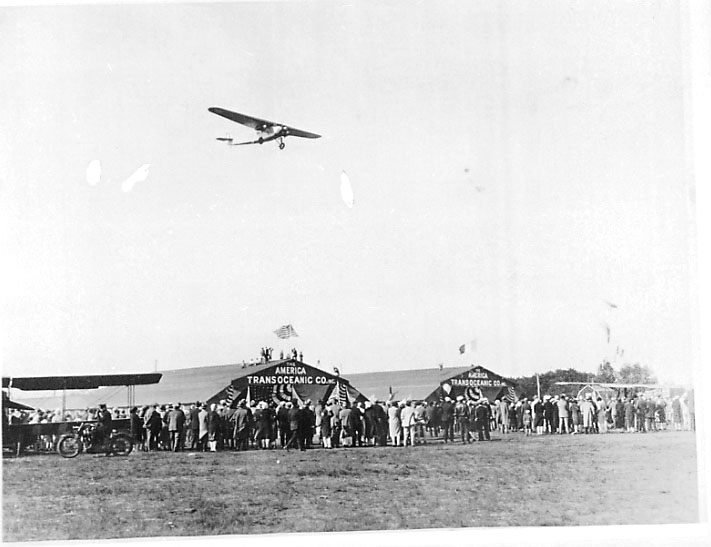 Lufthavn, 1 fly i lufta, Fokker C-2, C-2A "America". Bruker: Admiral Byrd. Mange personer foran hangarbygningert med påskrift "America Transoceanic Co. inc.