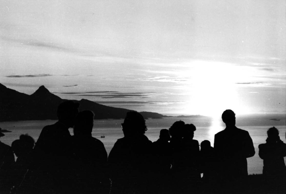 Flere personer i forgrunnen. Ser på solnedgangen i bakgrunnen. (SAS Midnattsolfly)