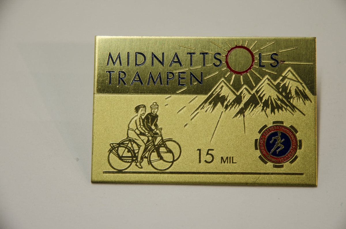 Idrottsplakett i metall med motiv av två cyklister, fjäll, sol och emblem; Svenska korporationsidrottsförbundet "Midnattssolstrampen 15 mil".