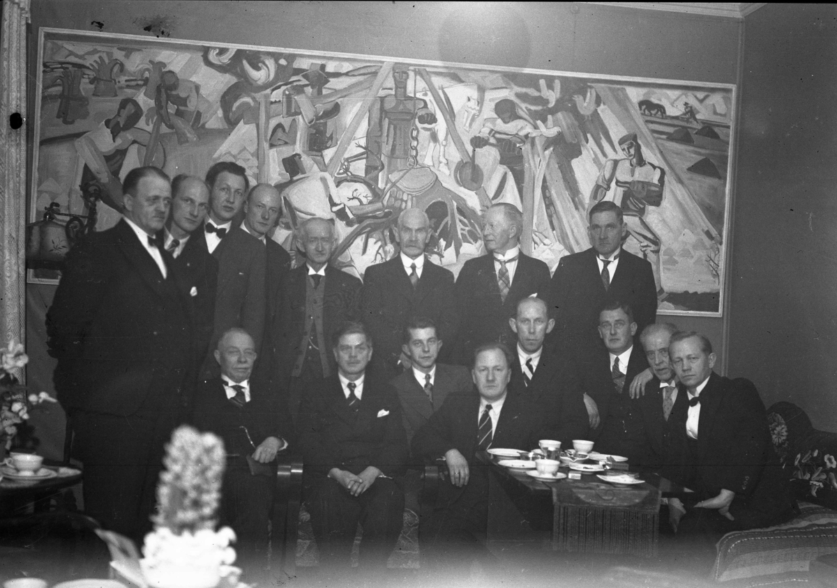 16 menn foran stort maleri med motiver fra arbeidslivet. 1938