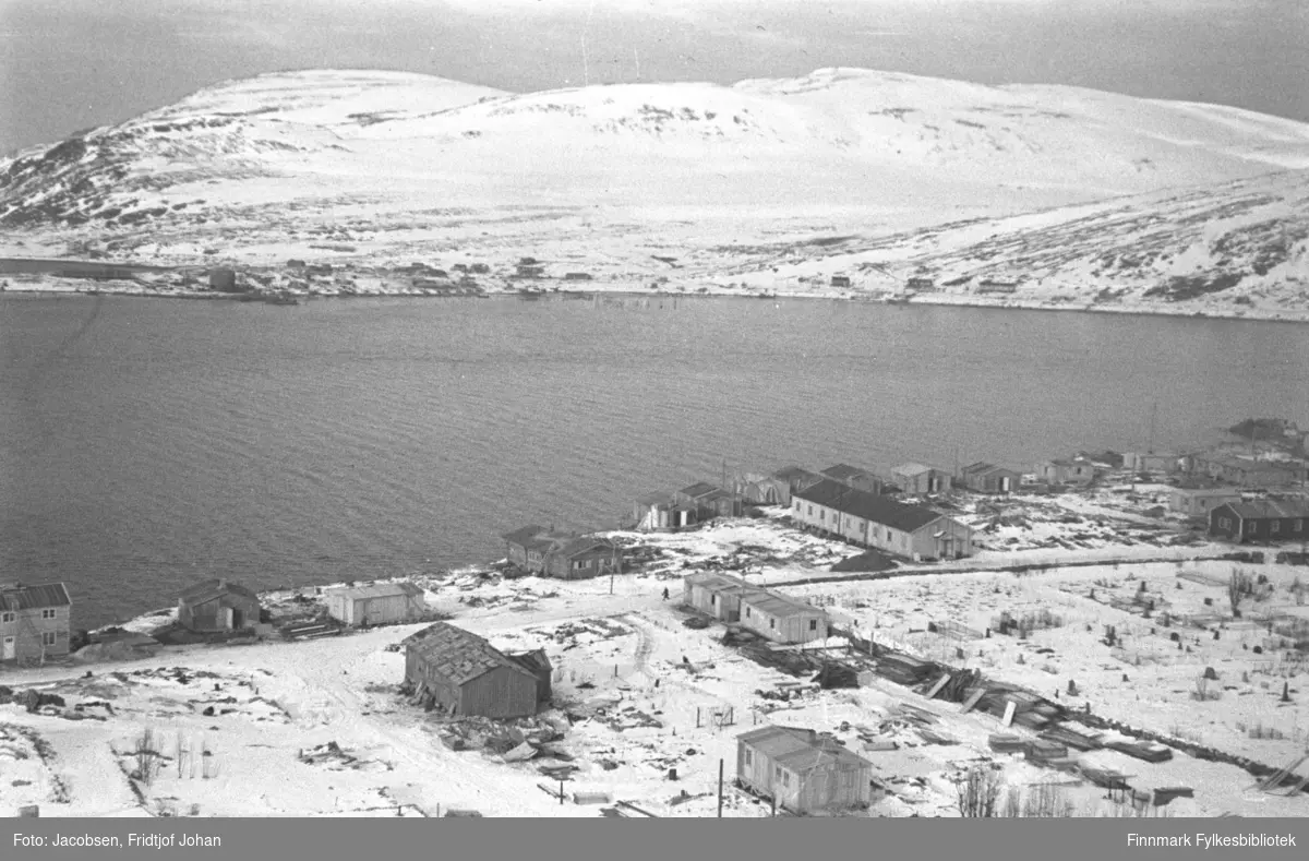 Bydelen Haugen i Hammerfest, høst/vinter 1945. Den lange, lyse brakka like nedenfor kirkegården, var FFR-brakka. Der FFR-brakka lå står i dag Hammerfest kirke. Gravlunden ligger til høyre i bildet og muren går langsmed der hvor FFR-brakka står. Noen flere brakker er satt opp på området som er delvis snødekt, men en del ruiner ses også. På andre siden av havna ligger bydelen Fuglenes. Noen brakker er satt opp der og, og saltsiloen ses ute på Fuglenesodden til venstre på bildet. Fjellet til venstre på bildet er Vardfjell med toppen av Vedhammeren bak. Midt på bildet er Storfjellet med Fuglenesdalen nedenfor.