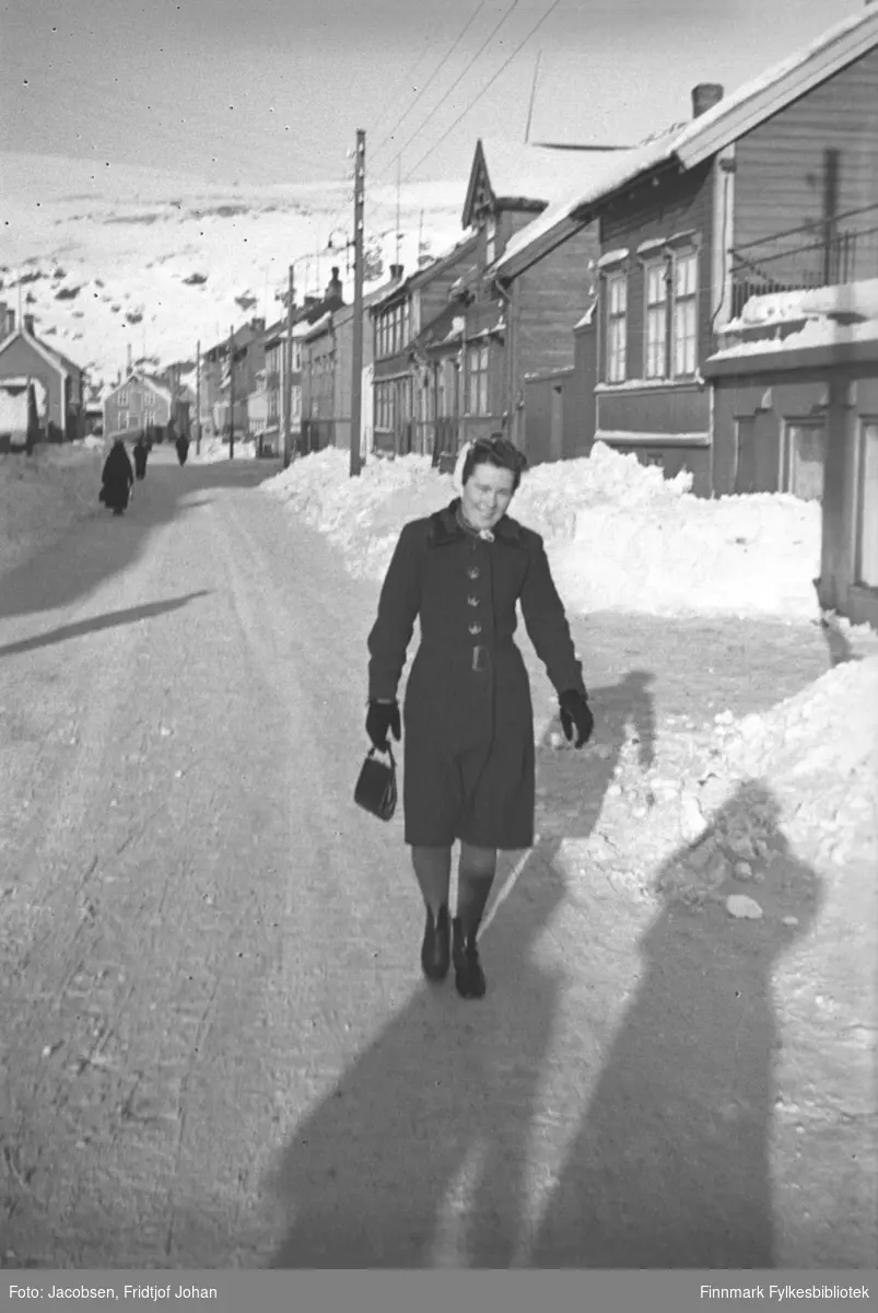 Karen Trondsen (Dalbom), fotografert i Nedre Grønnevoldsgate (i dag Strandgt.), i Hammerfest sentrum før 1940. Det er en fin vinterdag med sol, og fotografens skygge er synlig nede i høyre hjørne av bildet