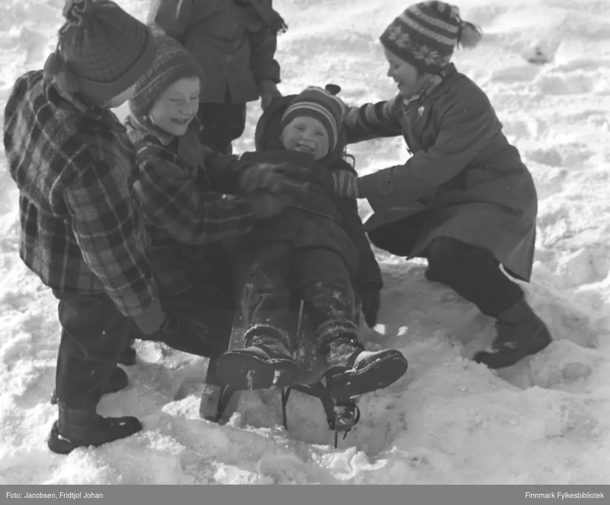 Barn leker i snøen på det islagte Storvannet. Alle har vinterklær, med luer og votter på seg. Et av barna ligger på en kjelke.