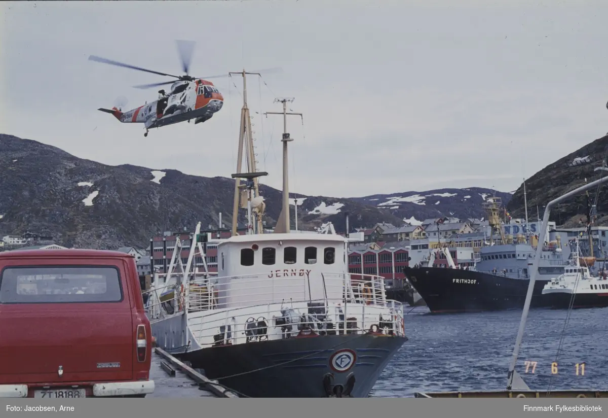 Et Sea-King redningshelikopter demonstrerer redning i Hammerfest indre havn. FFR-båten Jernøy ligger ved kai og over havna ligger Troms Fylkes Dampskibsselskap (TFDS) sin "Fjordkongen", utleid til FFR . (Det er to vesentlige ting som viser at dette ikke er et FFR fartøy, FFR hadde grå skrogfarge, mens båten på bildet er svart. Nummer to er den røde stripa som vises fra det tredje salongvinduet fra venstre. TFDS hadde røde striper på sine hurtigbåter. Rorhuset på "Brynilen" sto også noe lengre bak enn det gjorde på de fleste andre Westamaraner, grunnet lasterommet som var i forkant av brua.) Ved siden av den ligger et stort skip, Frithjof. Over baugen til den ser vi deler av Findus-anlegget og fjellet Salen bak. Til venstre i bildet står en Ford Transit varebil parkert på kaia og Mollajellet ses i bakgrunnen. Nede til høyre ses hekken på en annen båt, muligens FFR-båten Sørøy.