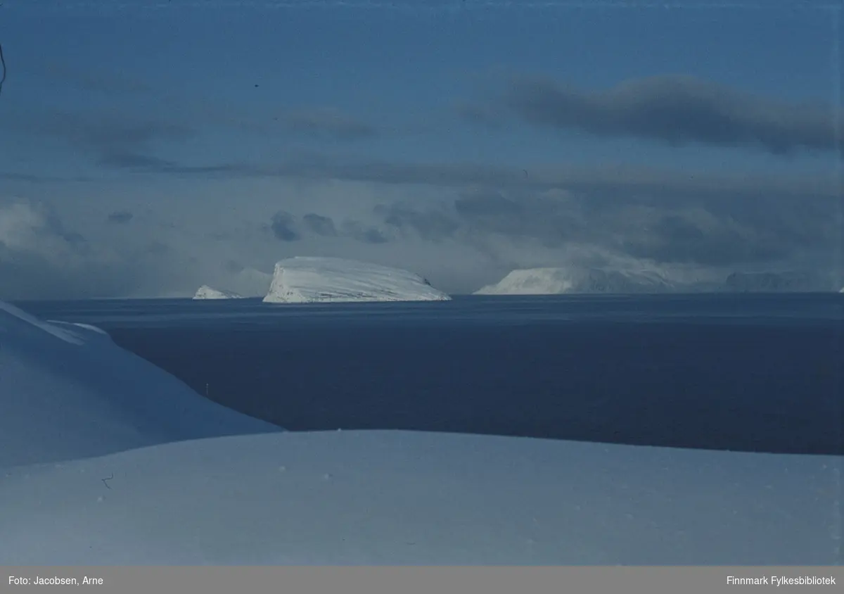 Midt i bildet ses øyene Håja med Hjelmen bak til venstre og Sørøya til høyre. Havområdet som vises er Sørøysundet. Det er mye snø. Oppholdsvær og lite vind. Bildet er tatt fra Bjørkåsen i Rypefjord utenfor Hammerfest