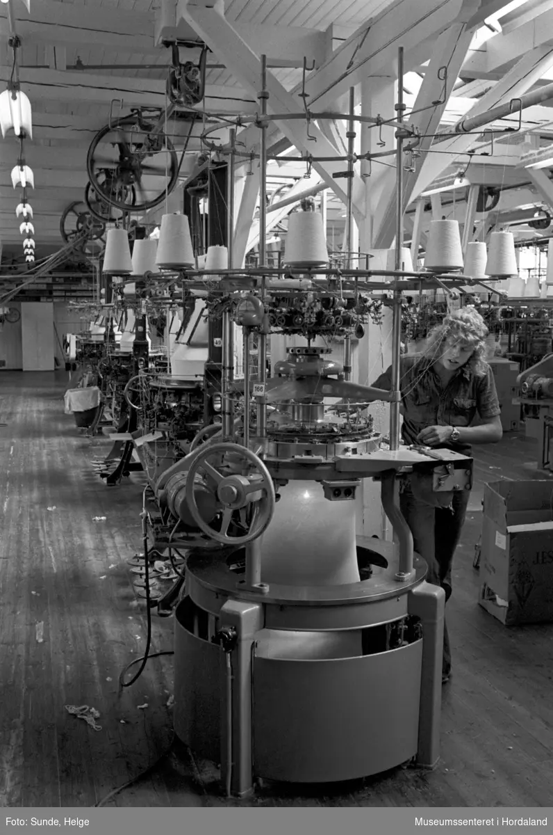 Arbeidsliv ved Salhus Tricotagefabrik i Salhus, Bergen i 1976. Arbeidar ved strikkemaskin på strikkeloftet på Salhus Tricotagefabrik.