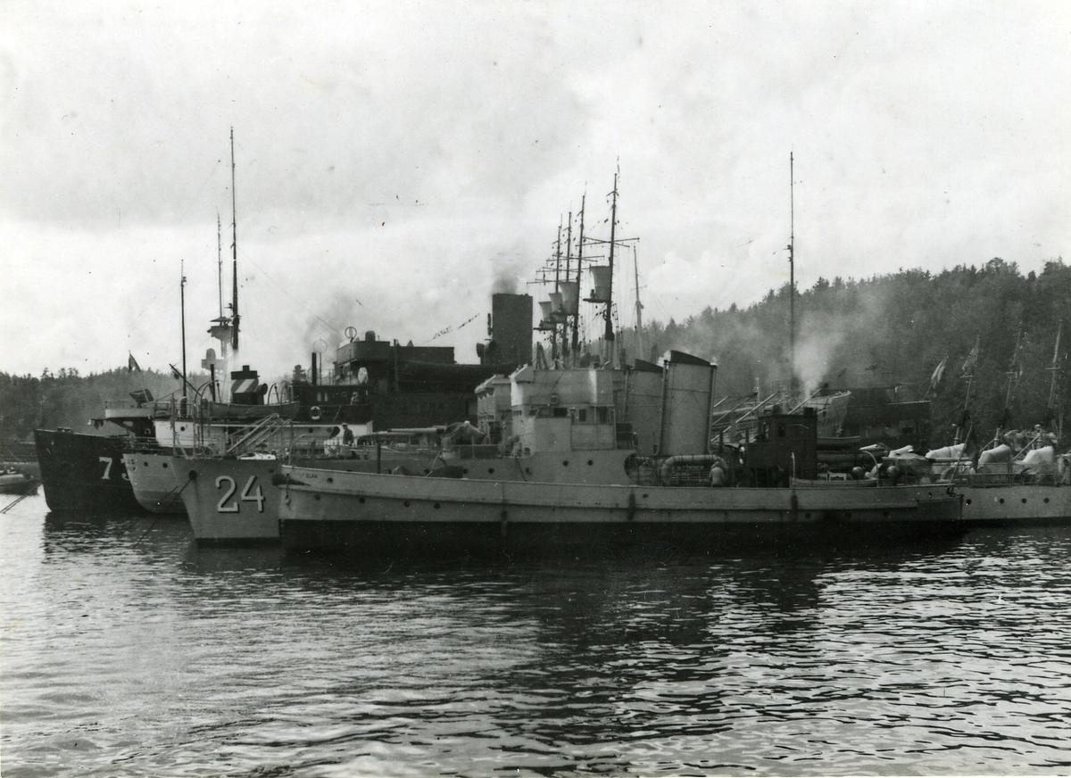 Olika typer av örlogsfartyg förtöjda ute i skärgård. Närmast pråmen Glan och torpedbåtar, längre bort stabsfartyget Marieholm.