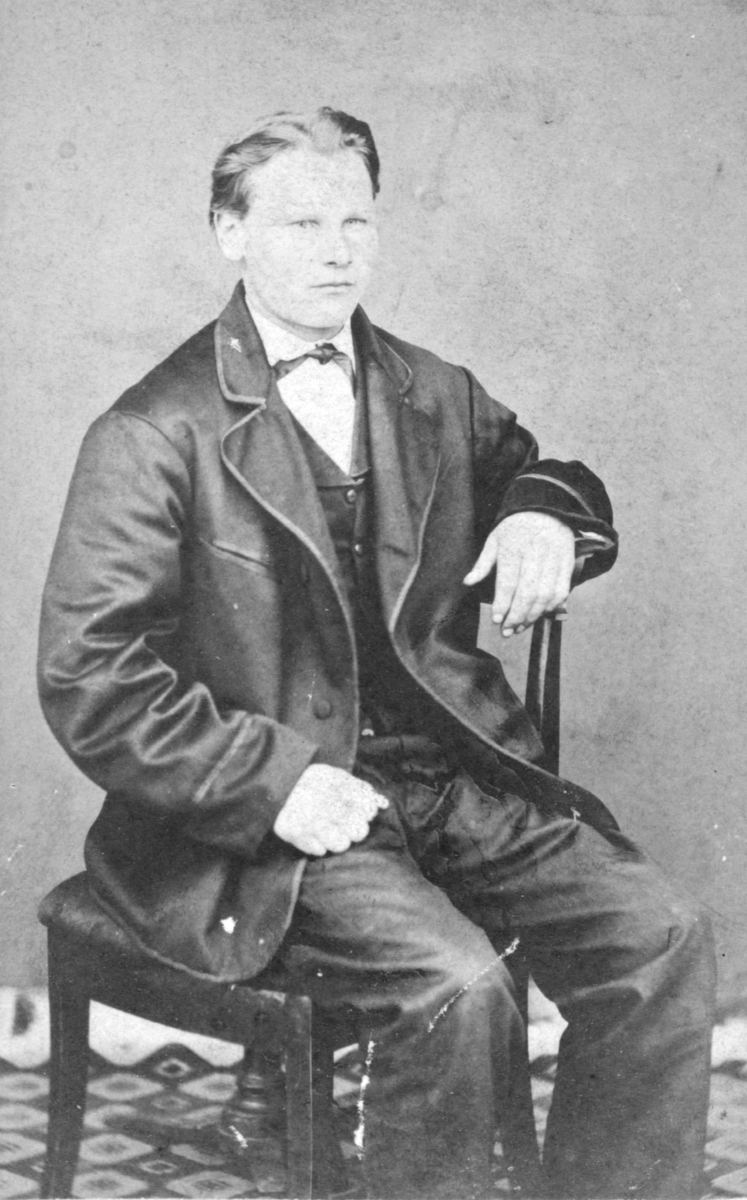 Et portrett av en ung mann, trolig av Johan Jonas. Han er kledd i jakke, vest, bukser, og har en søyfe rundt halsen. Han sitter på en stol. Bildet trolig tatt på slutten av 1800-tallet, begynnelsen av 1900-tallet.