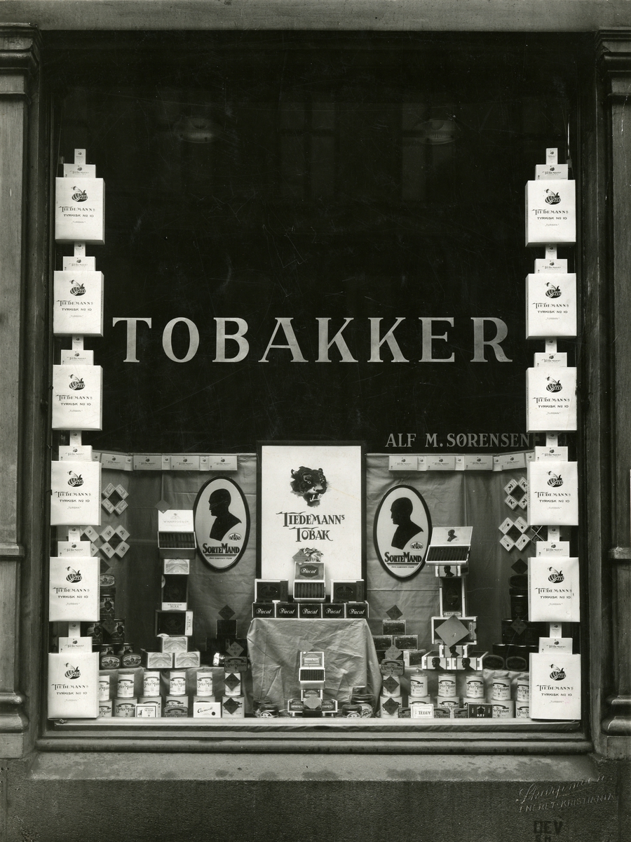 Vindusutstilling med reklame for produkter fra J. L. Tiedemanns Tobaksfabrik hos Alf M. Sørensen.