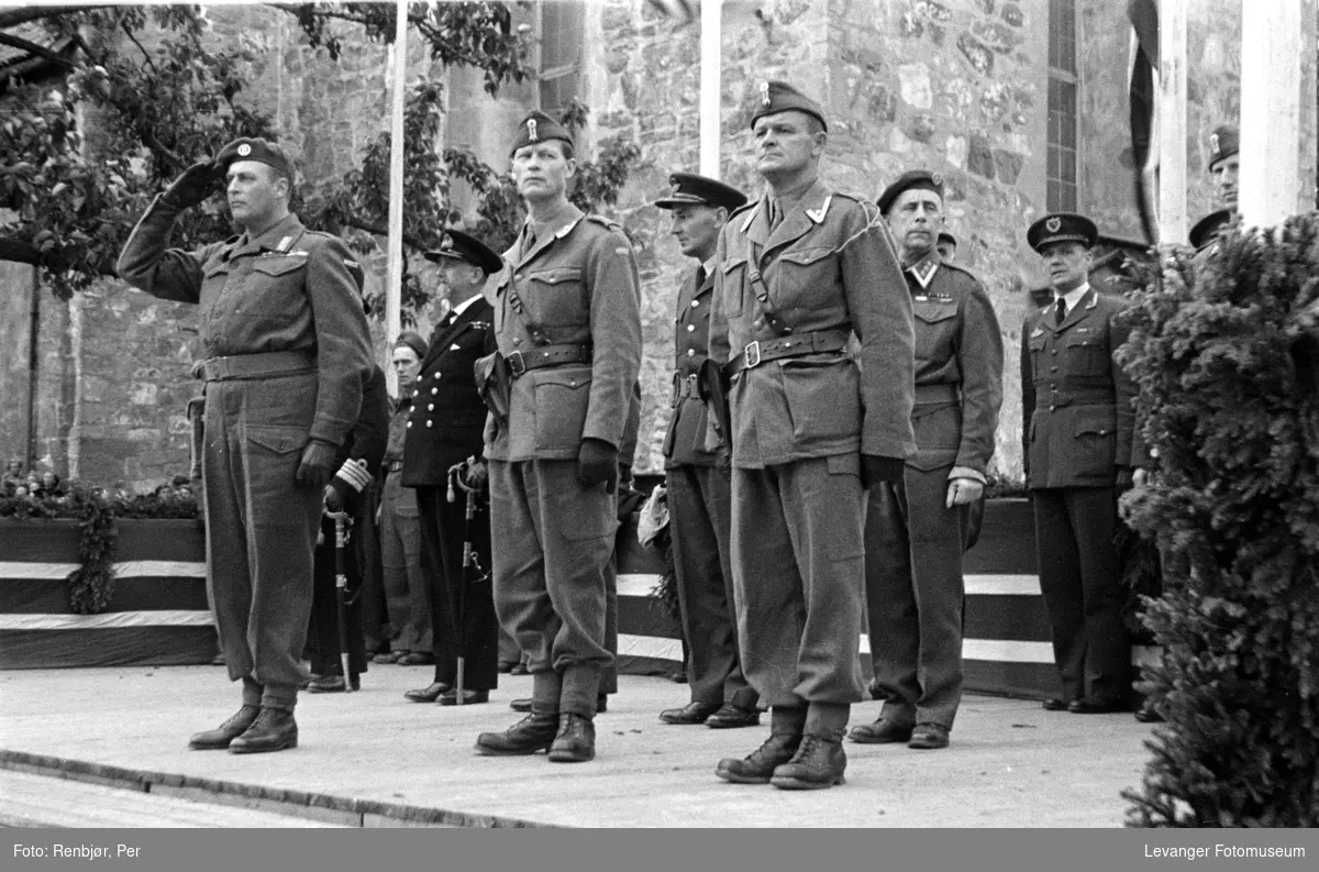 Kronprinsen salutterer soldatene på tribunen. med offiserer fra ulike våpengrener.