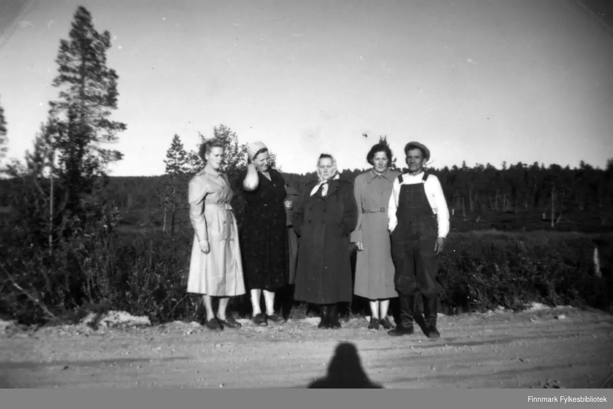 Fotografi av fire kvinner og en mann tatt på en grusvei. Fra venstre står Agnes Randa, Hilma Amanin, Maria Botti, Henrika Sotkajærvi og Alarik? Botti. Tre av kvinnene er kledt i kåper. Hilma bærer sin på armen. Hun har en mørk kjole på seg og et skaut på hodet. Alarik? er kledt i selebukse og lue. Det er skog i bakgrunnen
