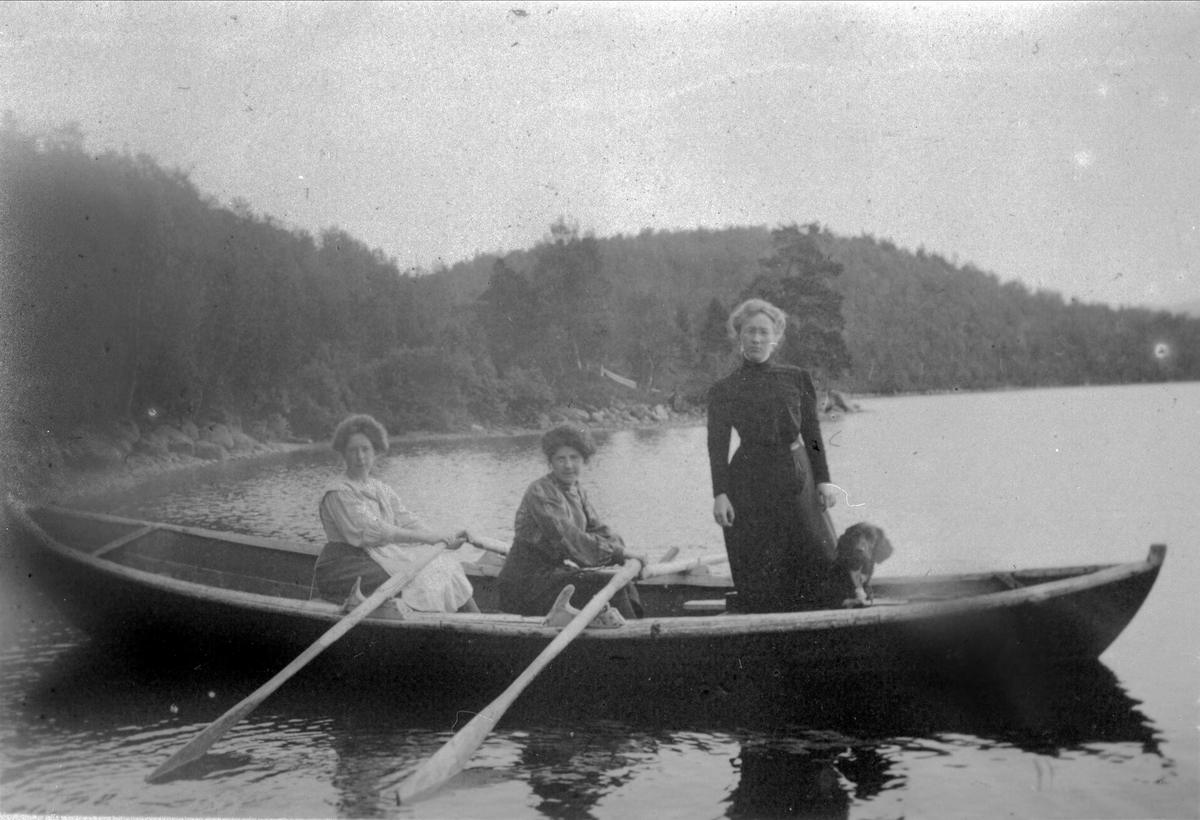 Tre kvinner og en hund i en robåt.