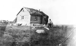 Mann med to barn foran tømmerhus med torvtak